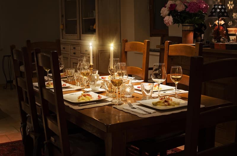 A wooden dinner table set for guests and lit by two candles